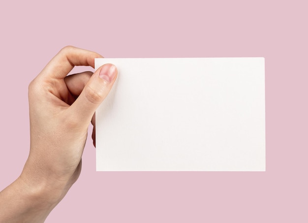 Biała pusta pusta pocztówka makieta w ręku na różowym tle