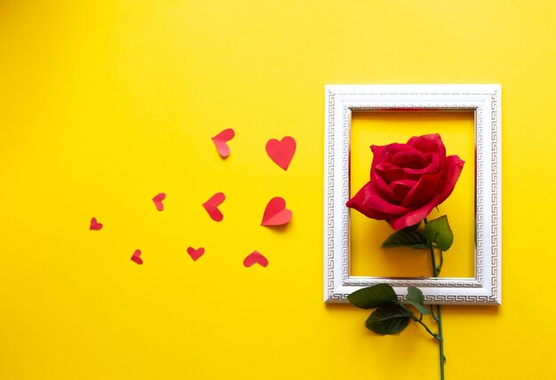 Biała ramka i serca w nim umieszczone na żółtym tle i czerwona róża. Walentynki tło.