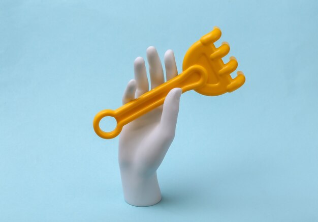 Biała Ręka Manekina Trzyma Grabie Zabawki Na Niebieskim Tle