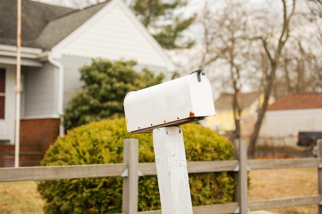 Biała skrzynka pocztowa stoi przed domem.