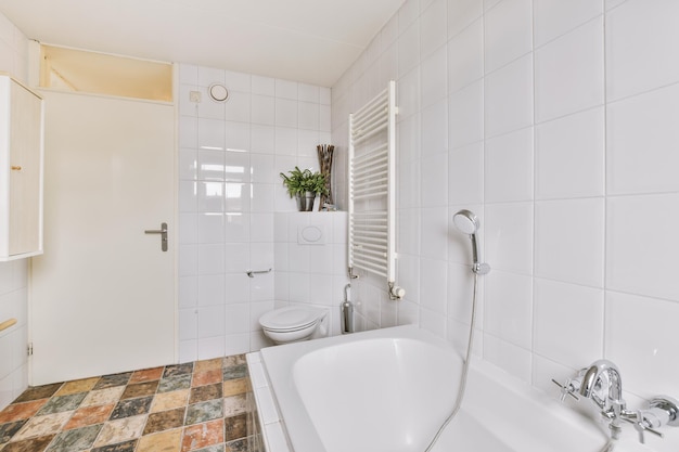 Biała wanna z metalowym kranem przy toalecie blisko drzwi w nowoczesnej łazience w minimalistycznym stylu w mieszkaniu