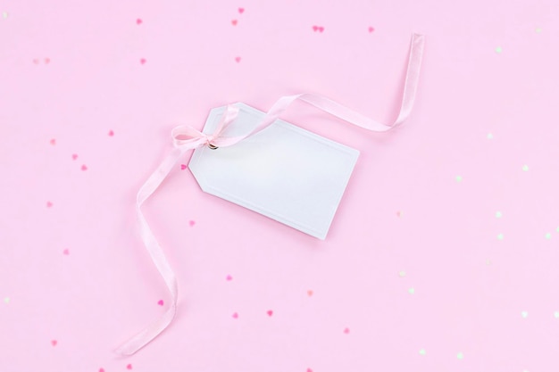 Biała zawieszka na prezent z różową wstążką na różowym tle z konfetti w kształcie serca