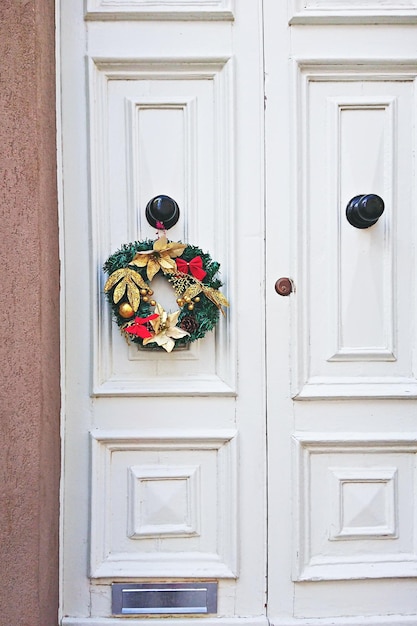 Białe drewniane drzwi wejściowe ozdobione świątecznym wieńcem w okresie świątecznym