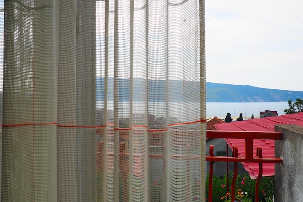 Białe firanki z grubej bawełny lub lnu wykonane ze splotów cienkich nici Proste kompaktowe ekonomiczne wnętrze mieszkania Dekoracja okna w pokoju Czerwony pasek Widok z pokoju hotelowego na brzeg morza