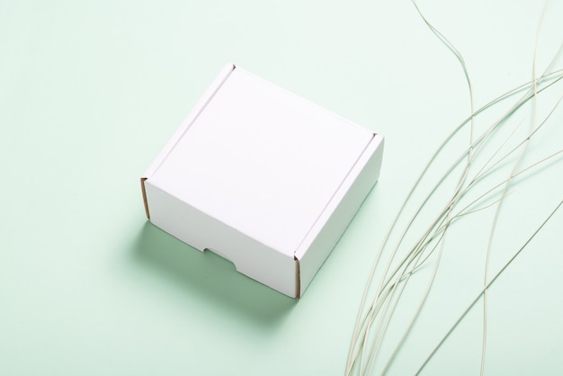 Białe kartonowe pudełko ozdobione liściem trawy