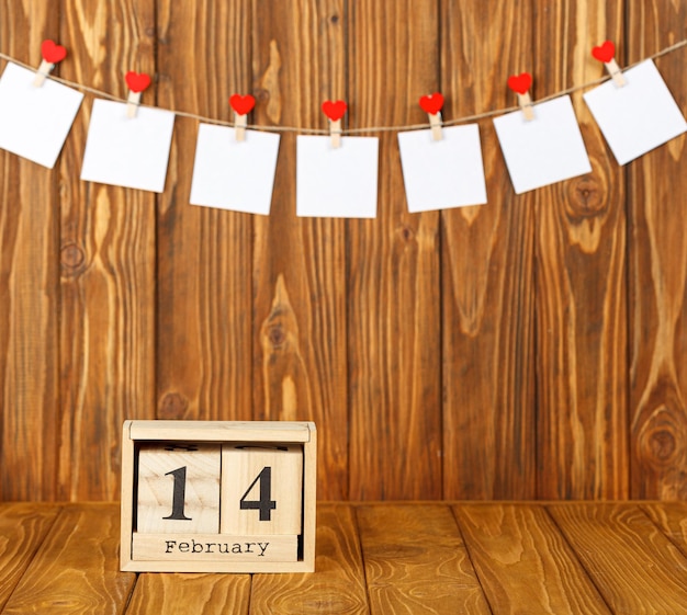 Białe kawałki papieru na spinaczach do bielizny z sercem na drewnianym tle kalendarza 14 lutego