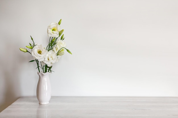 Białe kwiaty Eustoma lub Lisianthus w wazonie na jasnym drewnianym tle z miejscem na kopię