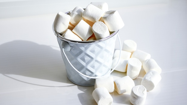 Białe mini marshmallows tło szczegół tekstura. Tło żywności. Skopiuj miejsce. Białe metalowe wiadro na białym tle