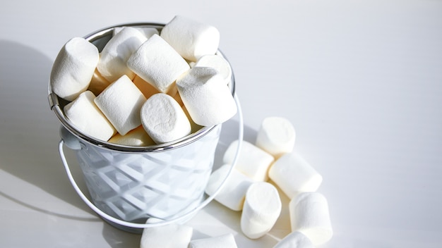 Białe mini marshmallows tło szczegół tekstura. Tło żywności. Skopiuj miejsce. Białe metalowe wiadro na białym tle