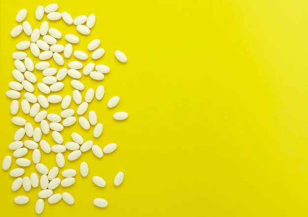 Białe owalne tabletki lub witaminy są rozrzucone na żółtym tle Płaski układ Przestrzeń kopii w widoku z góry