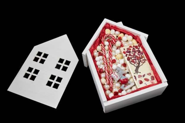 Białe pudełko w kształcie domu wypełnione słodyczami i tabliczką białej czekolady
