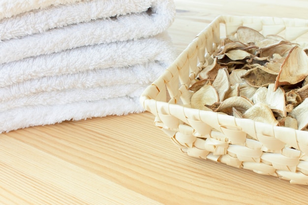 Białe ręczniki i kosz z pikantnymi suchymi roślinami na jasnym tle drewnianych