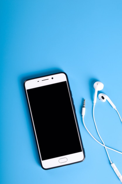 Białe słuchawki i smartfon na niebieskim stole, widok z góry