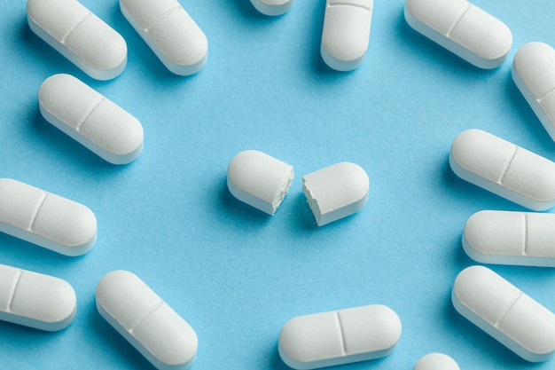 Białe tabletki na niebieskim tle. Jedna tabletka jest podzielona na pół, zmniejszając dawkę leku.