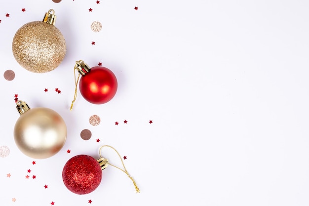 Białe tło bożonarodzeniowe ze złotymi i czerwonymi kulkami okrągłymi i gwiazdowym konfetti płaskim widokiem z góry z ok