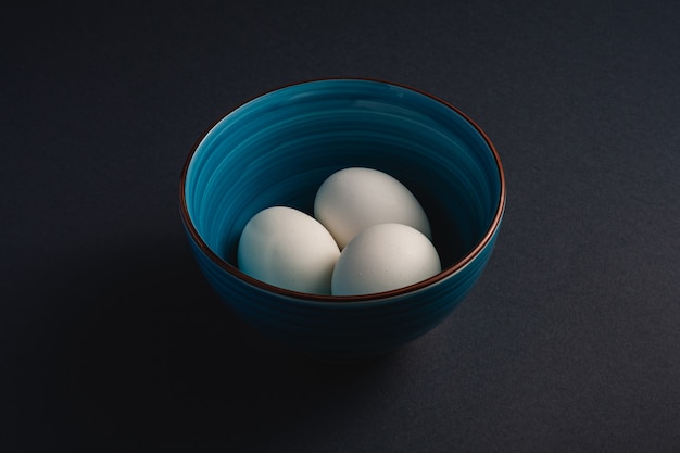Biali jajka w błękitnym pucharze na ciemnym markotnym czarnym prostym minimalnym tle, kąta widok, szczęśliwy Wielkanocny dzień