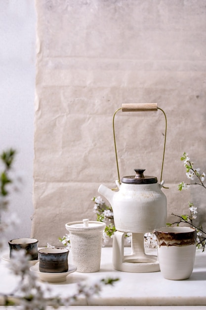 Biało-czarny ręcznie robiony ceramiczny czajnik z czarnymi ceramicznymi kubkami, dzbankiem katakuchi i kwitnącą wiśnią jako dekoracją stojącą na marmurowym stole. Tradycyjna japońska ceremonia parzenia herbaty. Teadrinking