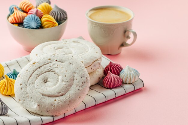 Biały bezowy ciasteczko na różowym tle z kolorowymi mini bezami