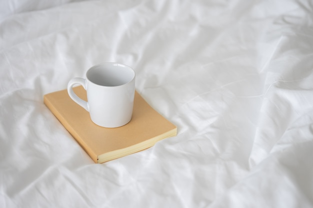Biały ceramiczny kubek do kawy umieszczony na brązowej okładce notebooka.