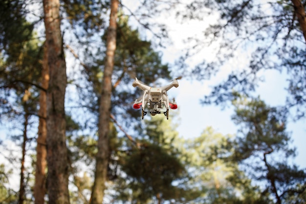 Biały Dron Unoszący Się W Lesie. Helikopter Dron Uav Latający Z Aparatem Cyfrowym.