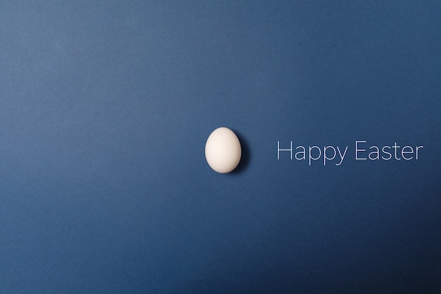 Biały Easter Jajko Z Szczęśliwym Easter Słowem, Wakacyjny Pojęcie. Niebieskie Tło.