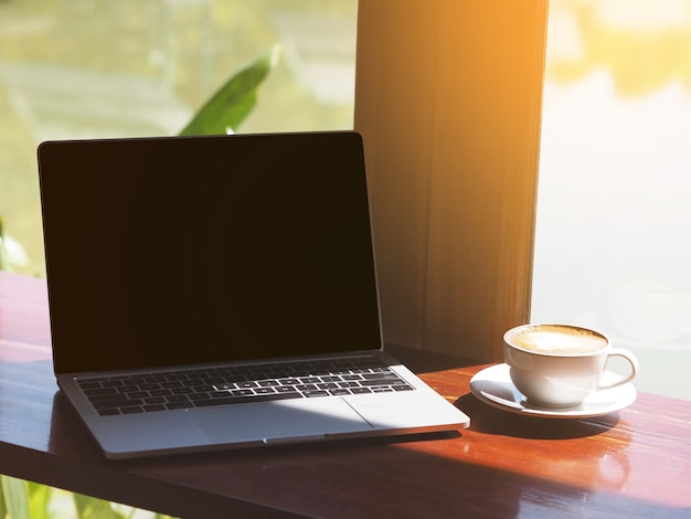 Biały filiżanka kawy cappuccino i laptop na stole obok szklanego okno