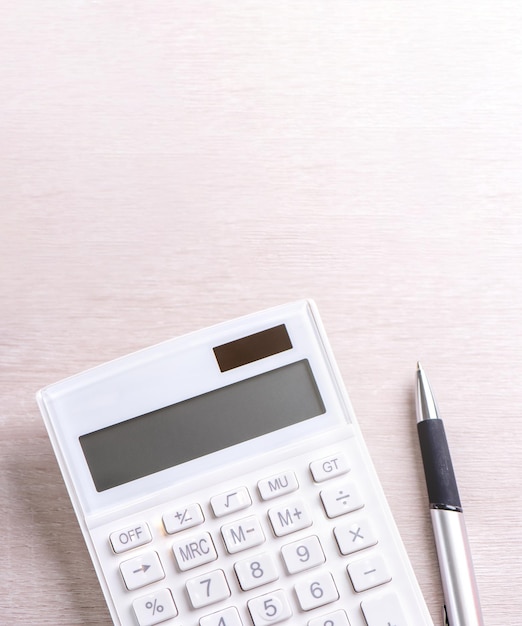 Biały kalkulator i długopis na jasnym drewnianym stole analizy i statystyki koncepcji ryzyka finansowego zysku inwestycyjnego skopiuj przestrzeń widok z góry płaski układ