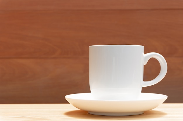 Zdjęcie biały kawowy kubek i spodeczek na drewnianym stole interliniujemy tło dla teksta