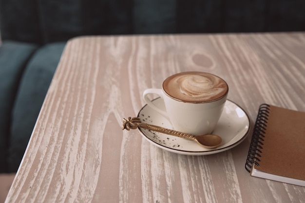 Biały kubek gorącego cappuccino na drewnianym jasnym tle stołu