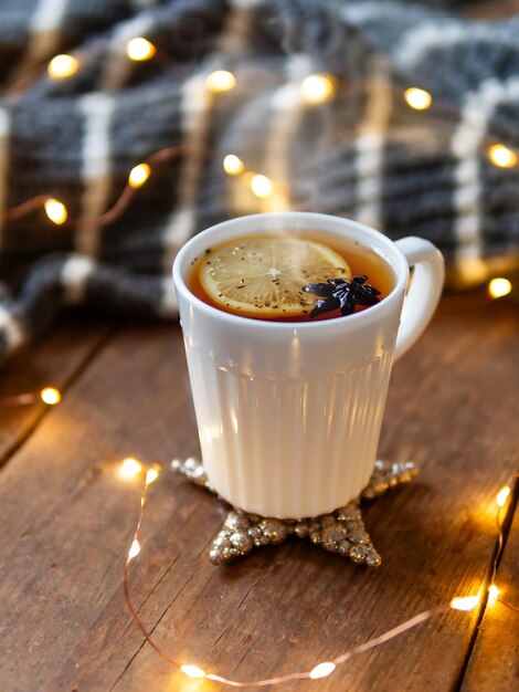 Zdjęcie biały kubek gorącej herbaty z cytrynowymi przytulnymi dekoracjami - szary dziany sweter i żarówki na drewnie