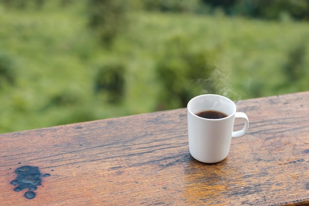 Biały kubek gorącej kawy lub herbaty na drewnianym stole rano z tłem gór i przyrody