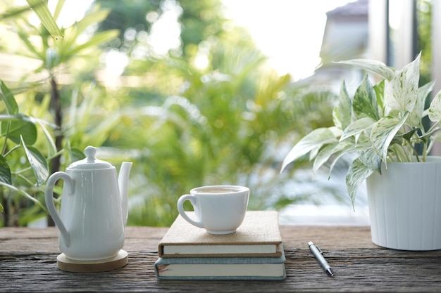 Zdjęcie biały kubek herbaty i garnek do herbaty oraz garnek do roślin i notatnik na drewnianym tacce i stole z widokiem na balkon na zewnątrz