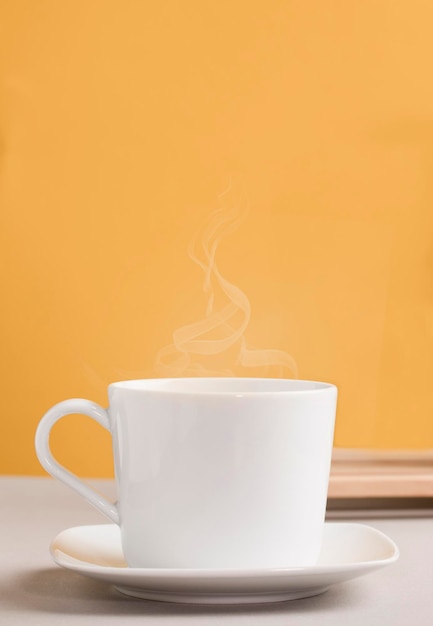 biały kubek z gorącym napojem kawa lub herbata z pomarańczowożółtym tłem