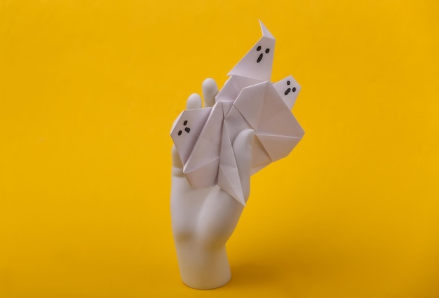 Biały manekin ręki trzymającej origami duchy na żółtym tle. Koncepcja Halloween