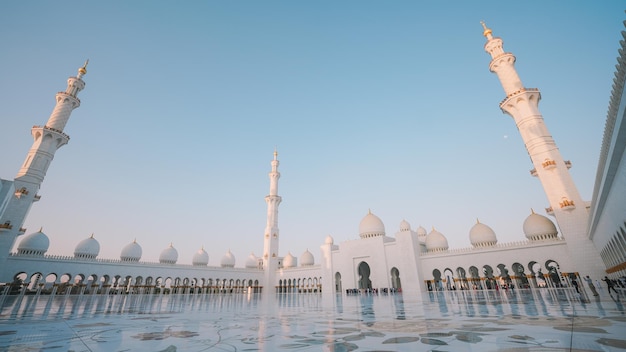 Biały meczet ze złotym posągiem na pierwszym planie i błękitnym niebem w tle.