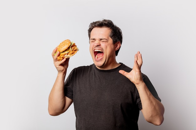 Biały mężczyzna w czarnej koszulce z burgerem na białej ścianie