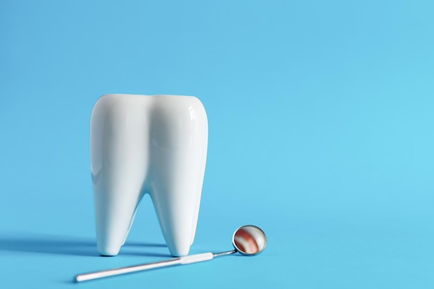 Biały model zęba dentystycznego z narzędziami stomatologicznymi do pielęgnacji zębów na niebieskim tle