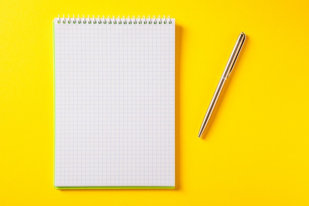 Biały otwarty notatnik na srebrnym piórze odizolowywającym na kolorze żółtym