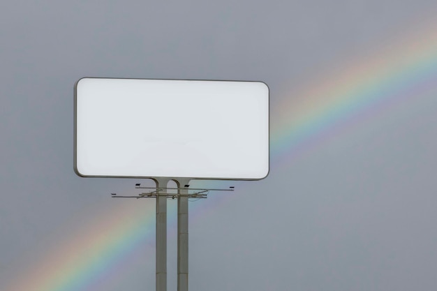 Biały prostokątny panel reklamowy z tęczą na niebie