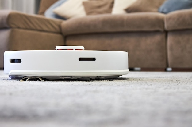 Biały robot odkurzający wykonuje automatyczne czyszczenie szarego dywanu w technologii Smart Home