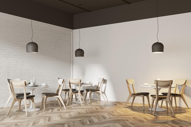 Biały róg kawiarni z drewnianą podłogą, okrągłe białe stoły i szare i drewniane krzesła.