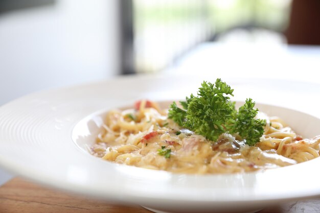 Biały sos do spaghetti (Spaghetti Carbonara) z boczkiem i czosnkiem, na tle drewnianego stołu