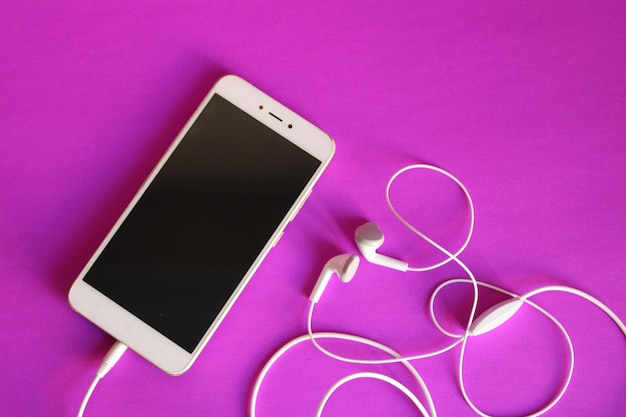 Biały telefon ze słuchawkami i fioletowym tłem.