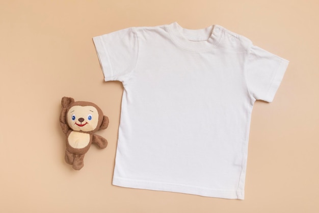 Biały tshirt dziecięcy widok z góry makieta na tekst logo lub projekt na beżowym tle Płaskie ubrania dla dzieci z zabawką