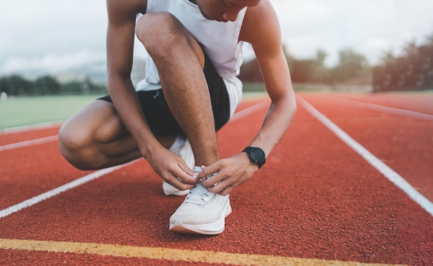 Biegacz człowiek klęczący i wiązanie sznurowadła na torze na stadionie sportowiec sportowiec przygotowuje się do treningu na wyścig konkurencja Sportowa koncepcja biegania
