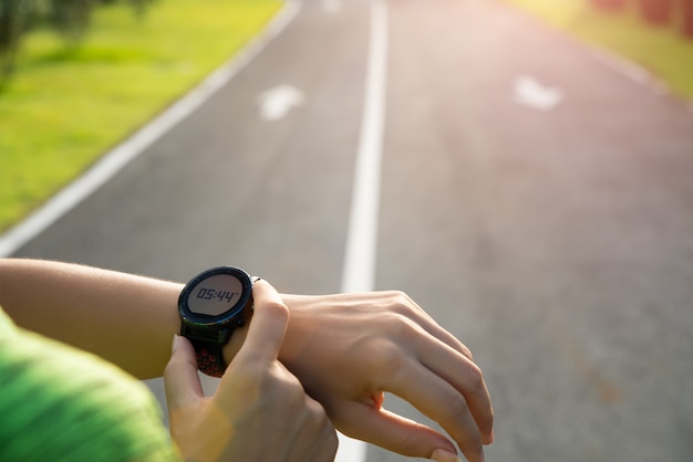 Zdjęcie biegacz konfiguruje inteligentny zegarek przed treningiem podczas zachodu słońca. ćwiczenie.