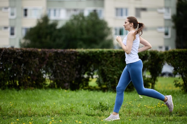 Biegacz ubrany w legginsy i białą koszulkę biegnie w zielonej okolicy dzielnicy mieszkalnej lub miasta