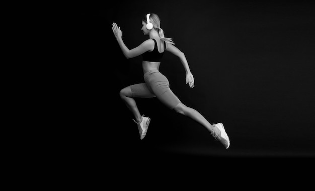 Biegnij ciężko, aby uzyskać kształt Kobieta biega na czarnym tle Skok joggera z długim biegiem Wysportowana atleta w modnym stroju sportowym Wysportowana sprinterka lub biegaczka Aktywna i dynamiczna Biegnij szybko finisz