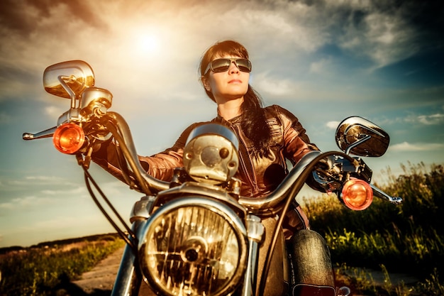 Biker dziewczyna w skórzanej kurtce na motocyklu patrząc na zachód słońca.