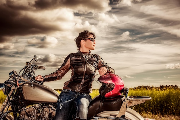 Zdjęcie biker dziewczyna w skórzanej kurtce na motocyklu patrząc na zachód słońca.